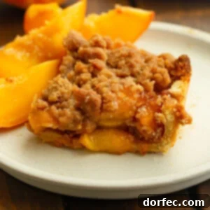 Another view of the peach crumble bar on a white plate with peach slices, highlighting the crisp streusel topping and thick peach layer.