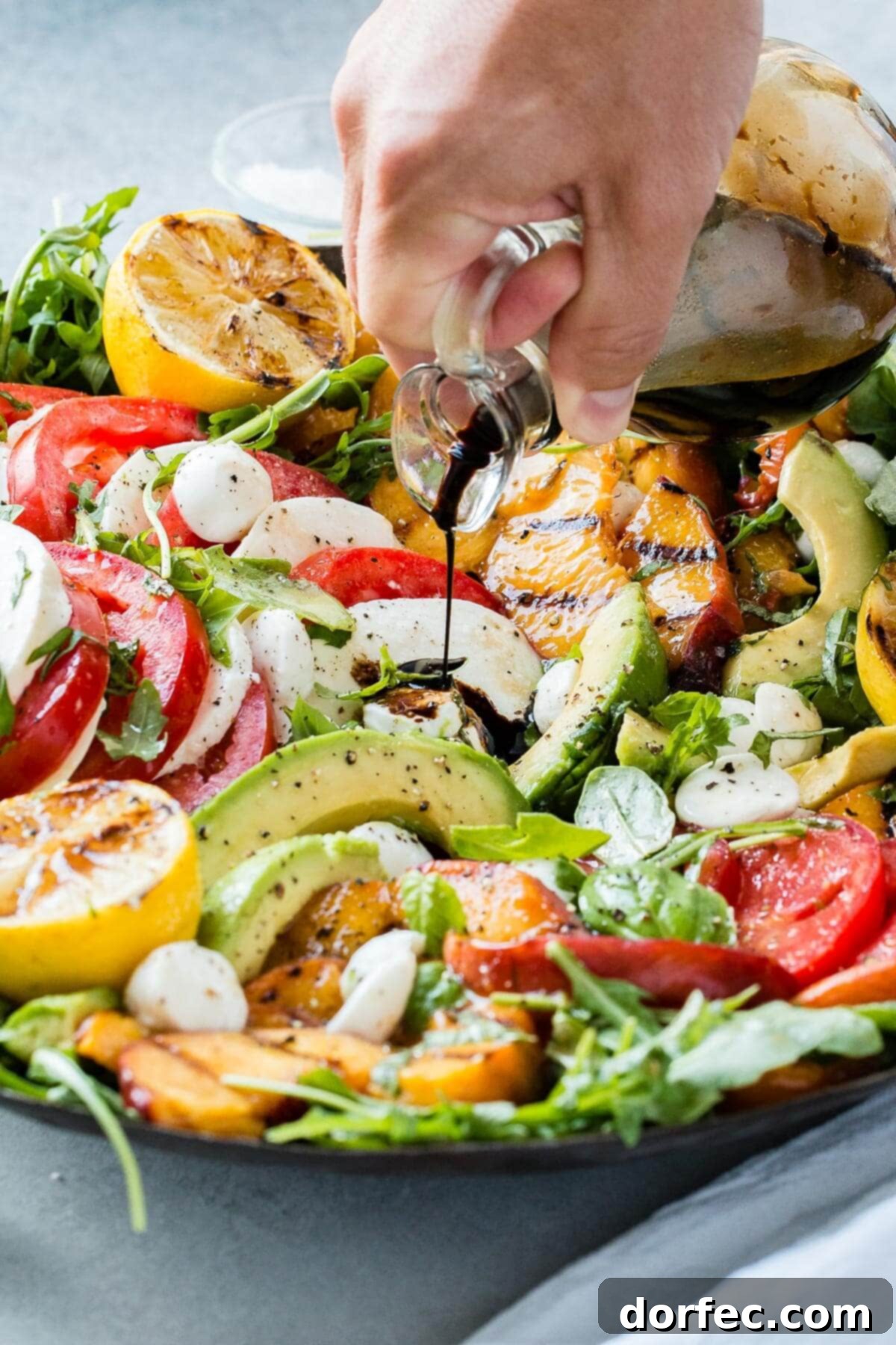 Sweet and Savory Grilled Peach Caprese 6 A hand drizzling balsamic glaze over the vibrant grilled peach Caprese avocado salad.