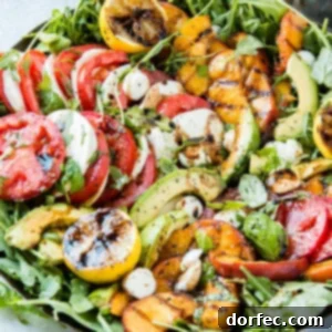 Close up of grilled peach caprese salad full of tomato slices, mozzarella slices, greens, and grilled peaches.
