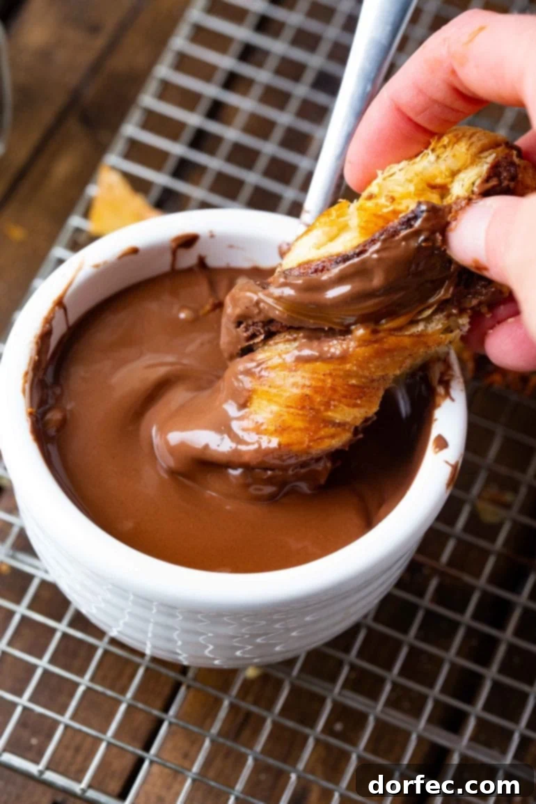 A photo of someone dipping a piece of a baked good into chocolate sauce, highlighting the deliciousness of the Nutella Dulce de Leche Christmas Tree.