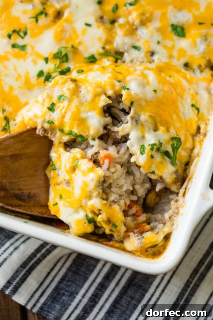 Hearty Cheesy Beef and Rice Bake 4 a white casserole dish with a ground beef, rice and carrot casserole with melted colby jack cheese on top and parsley for garnish.