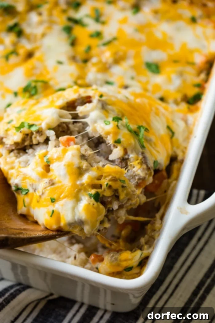 Hearty Cheesy Beef and Rice Bake 5 a wooden spoon scooping a ground beef, rice and carrots casserole with melted cheese on the top