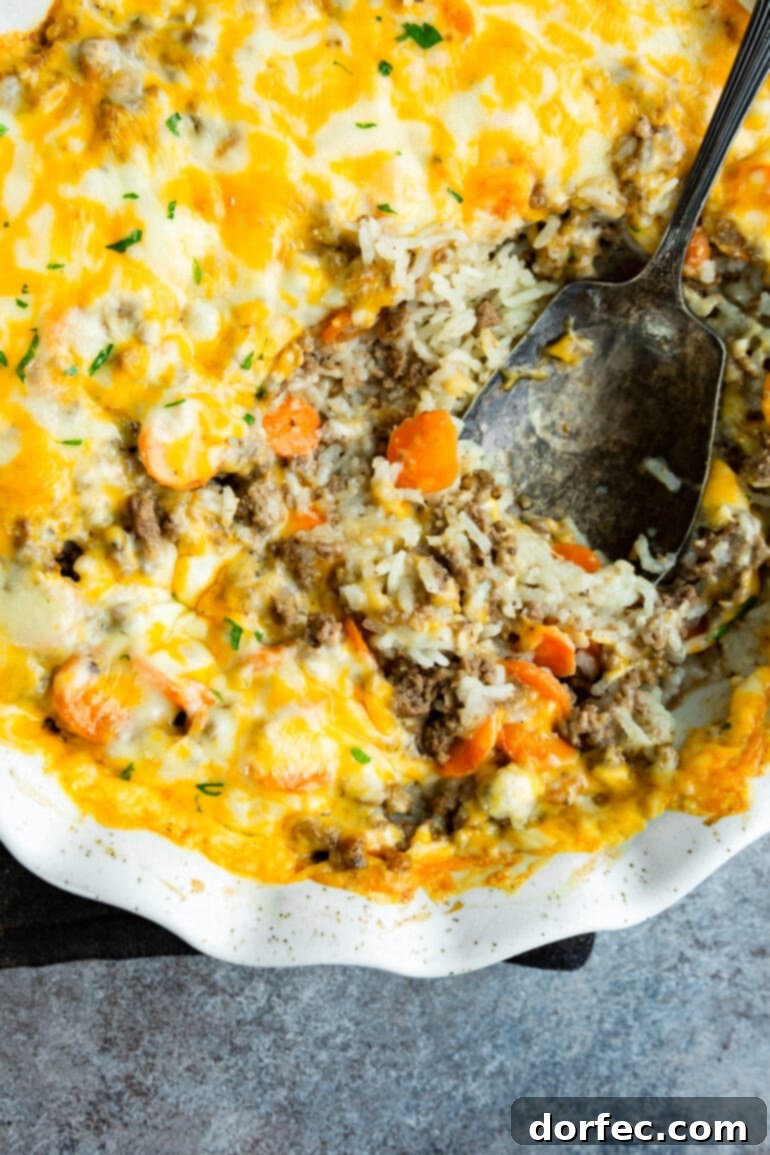 Hearty Cheesy Beef and Rice Bake 8 a photo of a ground beef and rice casserole topped with melted cheese and a large serving spoon digging into the casserole.