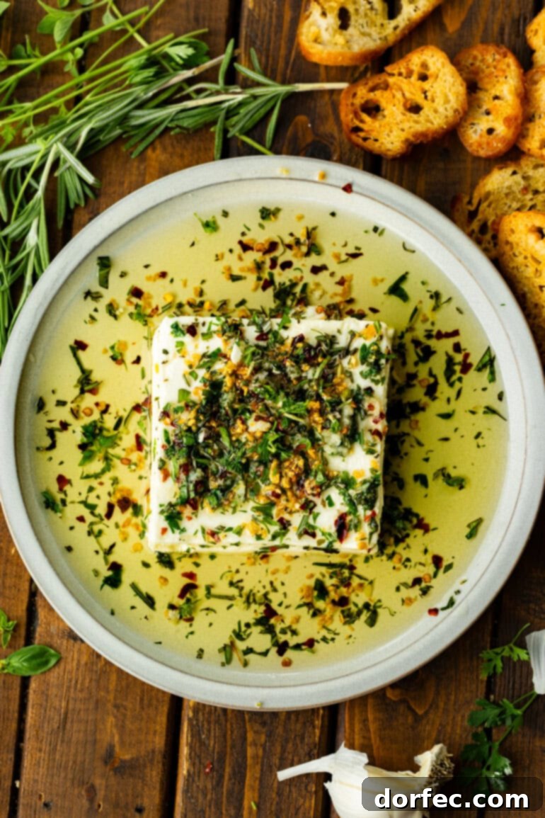 A square block of creamy feta cheese sitting on a elegant serving plate, surrounded by a luscious pool of herby olive oil, ready for dipping.