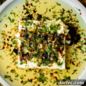 A top-down view of a sizzling oil Greek feta dip in a small white bowl, ready to be served with crostini.