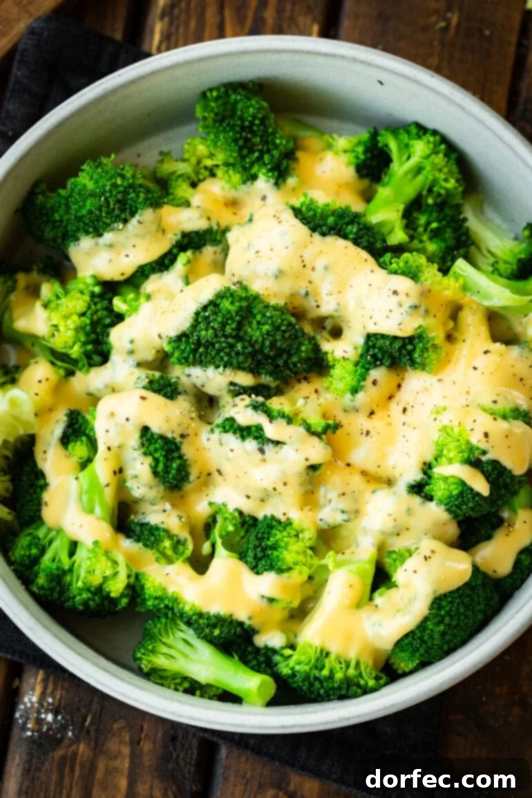 A large bowl of bright green steamed broccoli topped with rich cheddar cheese sauce and a sprinkle of salt and pepper, ready to be served.