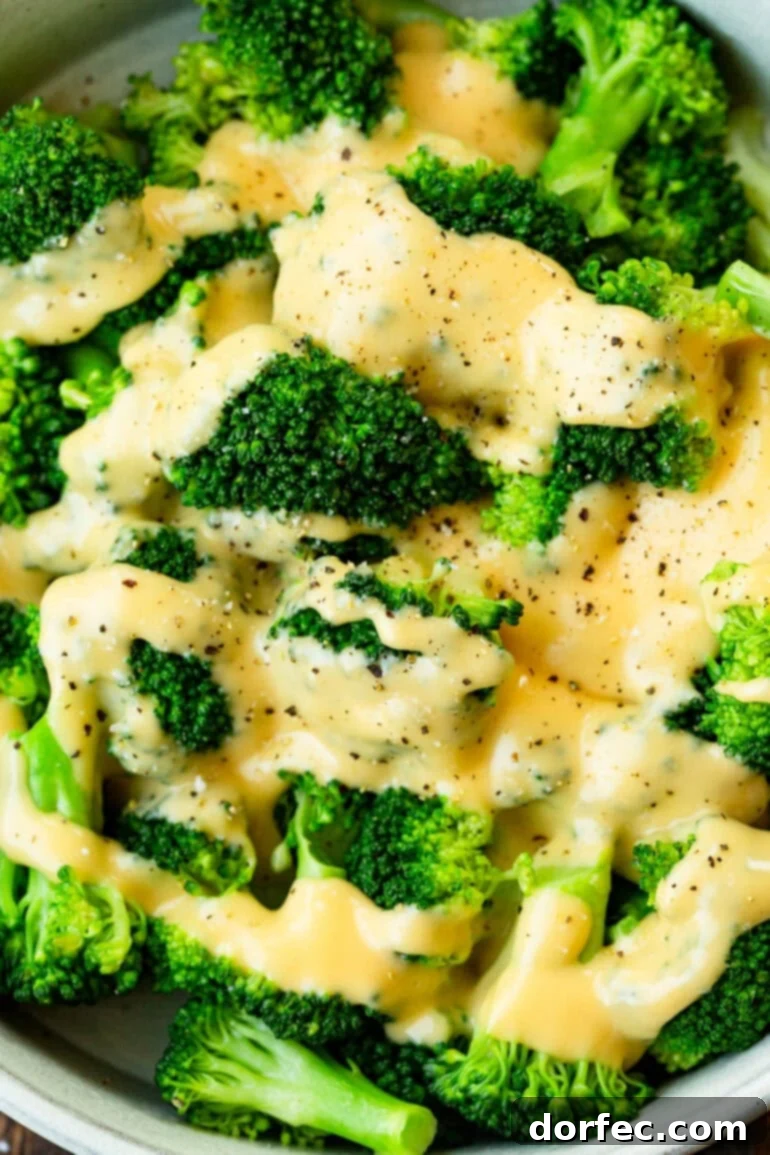 Close-up of bright green broccoli florets generously coated with creamy cheddar cheese sauce, seasoned with salt and freshly cracked black pepper.