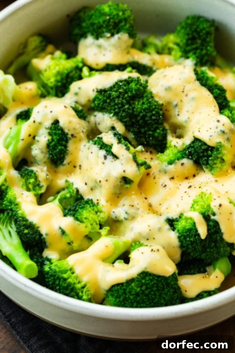 Creamy cheddar cheese sauce generously poured over a serving of freshly steamed broccoli, lightly sprinkled with fresh black pepper for garnish.