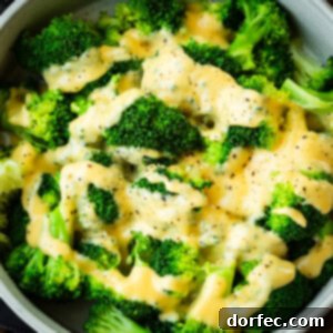 A large bowl of bright green steamed broccoli topped with a creamy cheese sauce and sprinkled with salt and pepper.