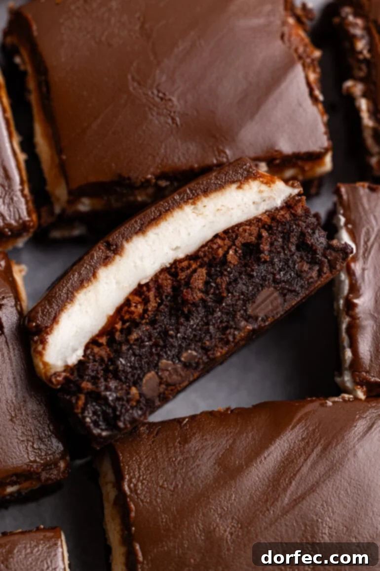 Several peppermint brownies, with one turned on its side to show the distinct fudgy chocolate, creamy peppermint, and glossy chocolate glaze layers.
