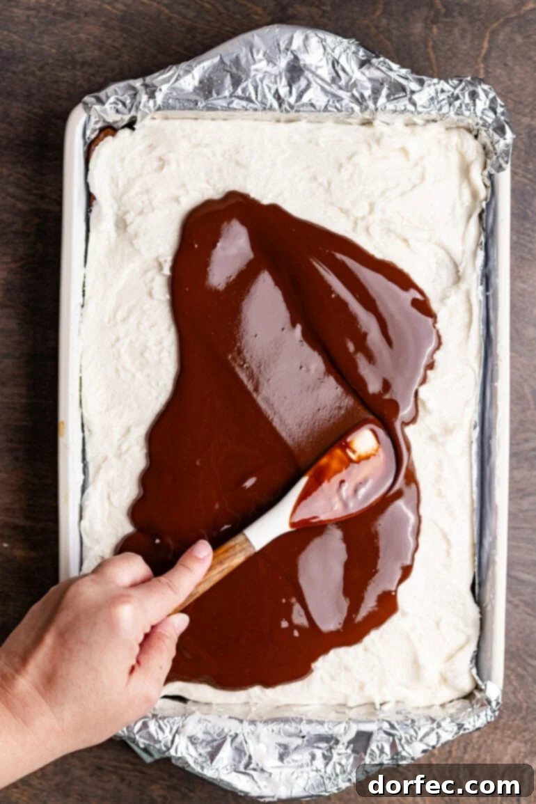 Pouring chocolate glaze over the peppermint layer on the brownies.