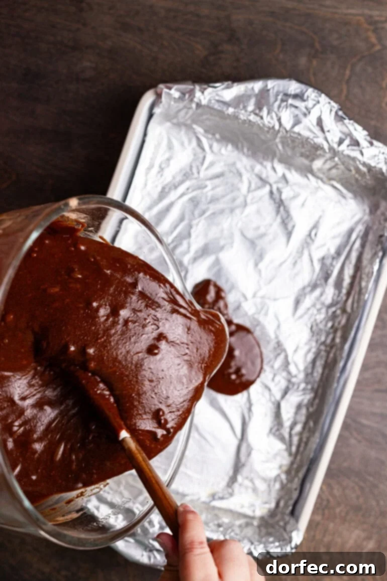 Pouring brownie batter into a prepared baking pan.