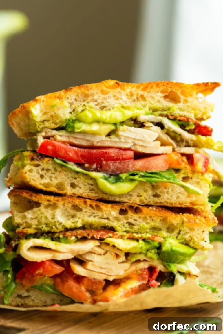A perfectly halved Turkey Bacon Avocado Sandwich, revealing abundant layers of turkey, crispy bacon, ripe avocado, fresh tomato, and vibrant greens, all nestled within a sturdy, wholesome bread, ready to be enjoyed.