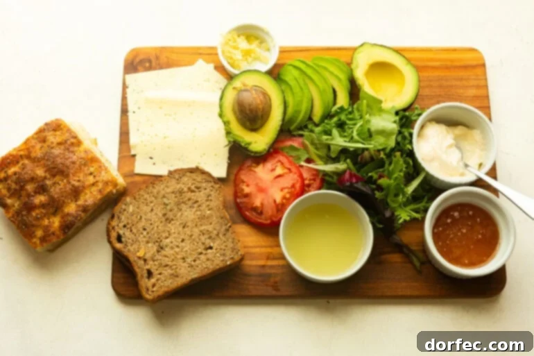 All the fresh ingredients for a Turkey Bacon Avocado Sandwich neatly arranged on a rustic wooden cutting board, including slices of turkey, crispy bacon, ripe avocados, juicy tomatoes, and a bowl of the creamy honey avocado spread.