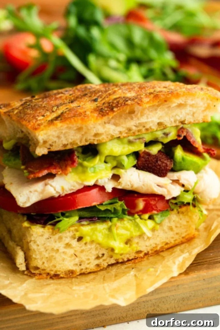 A vibrant and generously filled half of a Turkey Bacon Avocado Sandwich on focaccia bread, showcasing luscious avocado sauce, ripe tomatoes, crisp lettuce, tender thick turkey slices, and perfectly crunchy bacon.