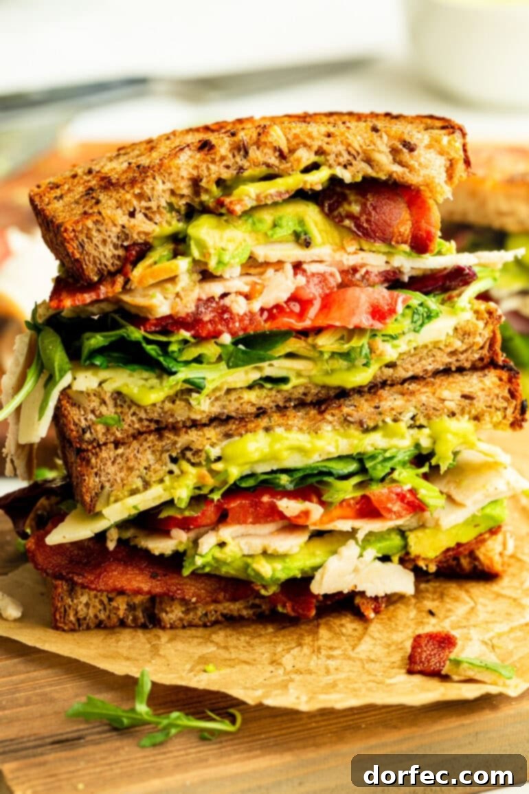 Two halves of a perfectly built Turkey Bacon Avocado Sandwich on wholesome multigrain bread, neatly stacked, showcasing the layers of fresh ingredients and creamy sauce.