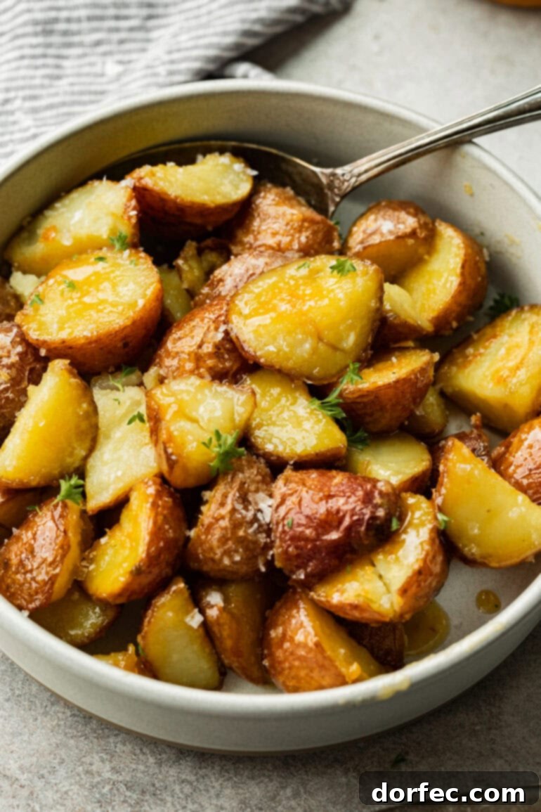 Perfectly Roasted Red Potatoes 4 Crispy, caramelized red potatoes resting in a minimalist white bowl, their golden edges contrasting beautifully with the smooth surface beneath, highlighted by fresh green herbs.