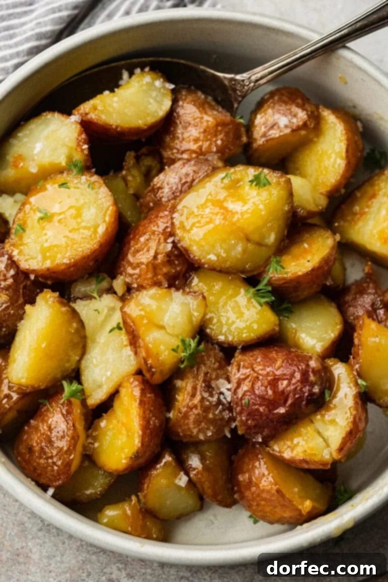 Perfectly Roasted Red Potatoes 6 Golden, crispy roasted red potatoes piled high in a clean white bowl with a silver spoon, glistening with honey butter and sprinkled with flaked sea salt, invitingly presented.