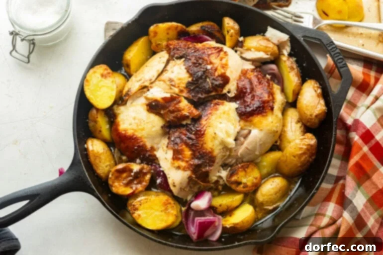 One Pan Garlic Butter Chicken and Potatoes 3 A whole roasted chicken with golden, crispy skin, a slice cut off to reveal the juicy meat, surrounded by roasted potatoes in a large cast iron skillet.