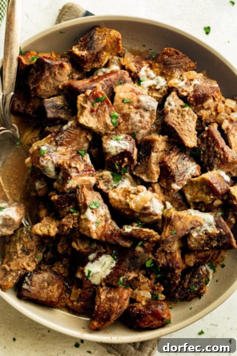 Effortless Garlic Butter Slow Cooker Steak Bites 5 A close-up of succulent steak bites coated in rich garlic butter, mingled with tender diced onions, and garnished with fresh chopped parsley in a serving bowl.