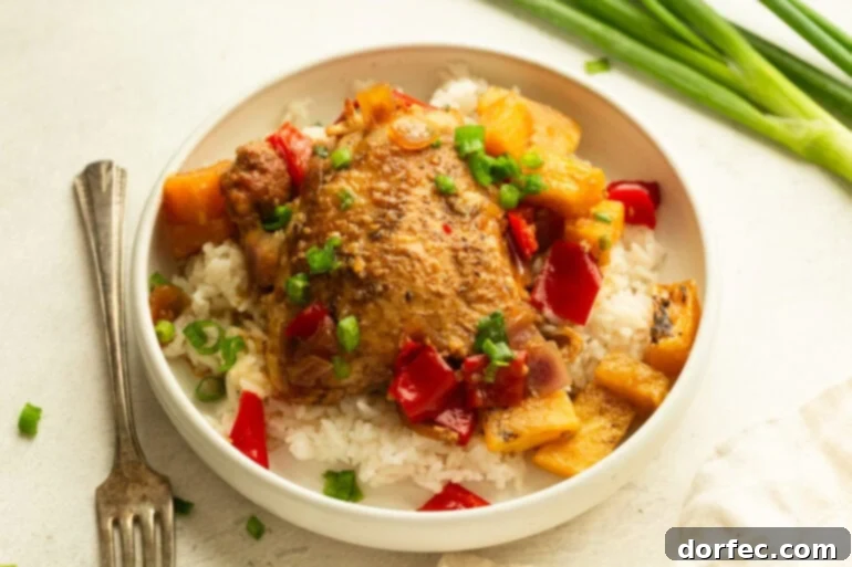 A serving of white rice topped with a golden chicken thigh, pineapple chunks, chopped red bell pepper and onions, showcasing the vibrant colors and appealing texture of the dish.