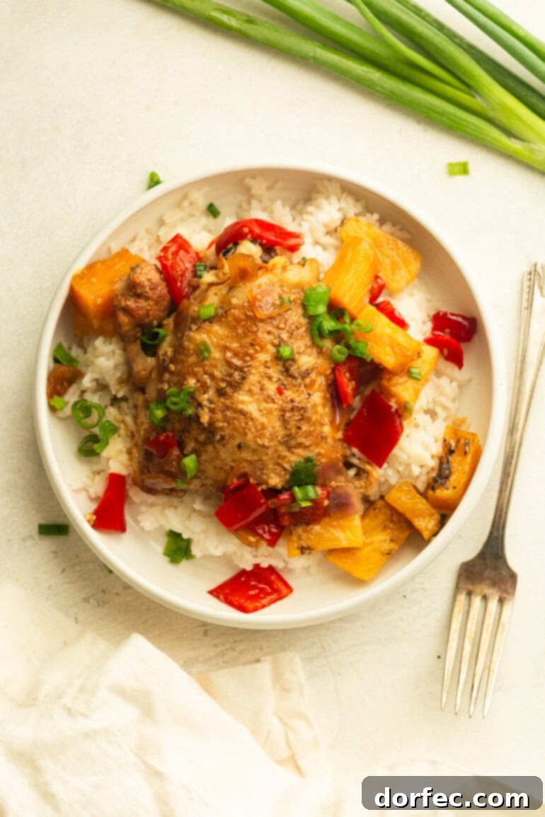 A pristine white plate featuring a generous serving of fluffy white rice, topped with a succulent golden chicken thigh, adorned with saucy pineapple, vibrant red bell pepper, and tender onions, all garnished with freshly chopped green onions.
