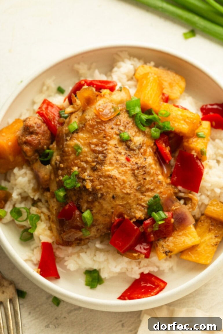 A beautifully presented dinner plate featuring a bed of white rice, topped with a succulent BBQ teriyaki chicken thigh, accompanied by vibrant pineapple, bell peppers, and onions, creating a mouth-watering tropical meal.
