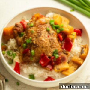 A serving of white rice topped with a golden chicken thigh, pineapple chunks, chopped red bell pepper and onions, ready to be enjoyed.