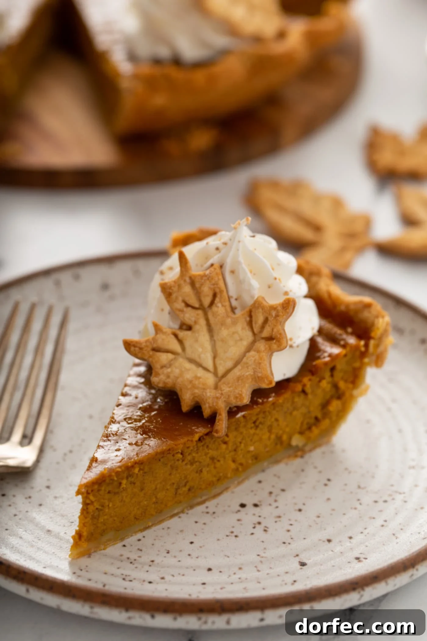 A single, delectable slice of homemade pumpkin pie, adorned with elegant piped whipped cream and a decorative pie crust leaf, perfectly presented.