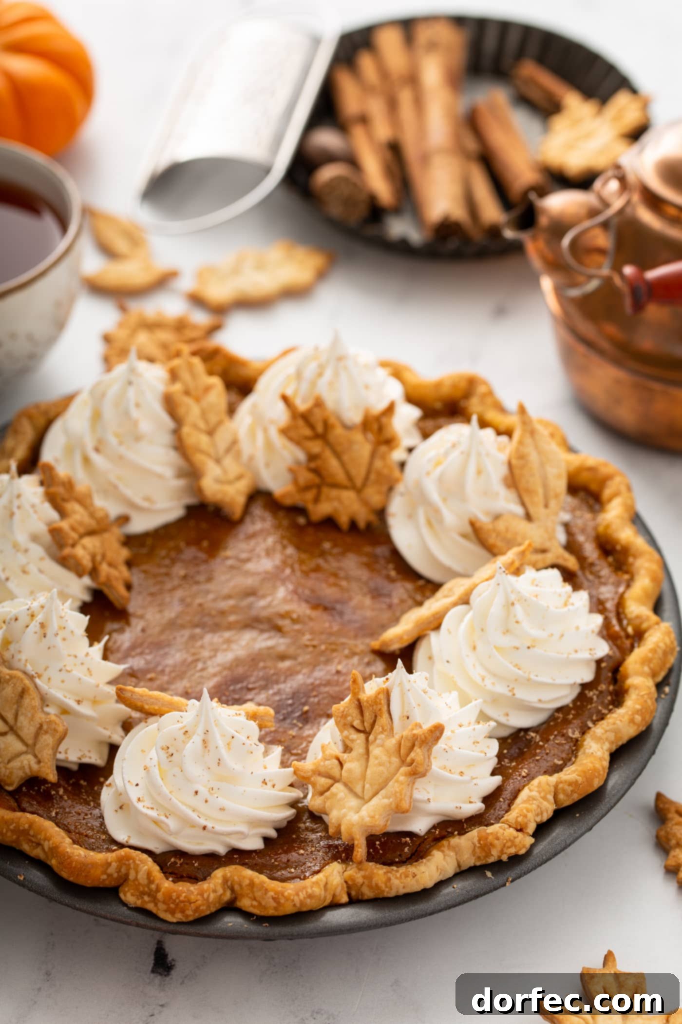 A beautifully baked whole classic pumpkin pie, generously topped with delicate piped whipped cream and charming pie crust leaves, ready for serving.