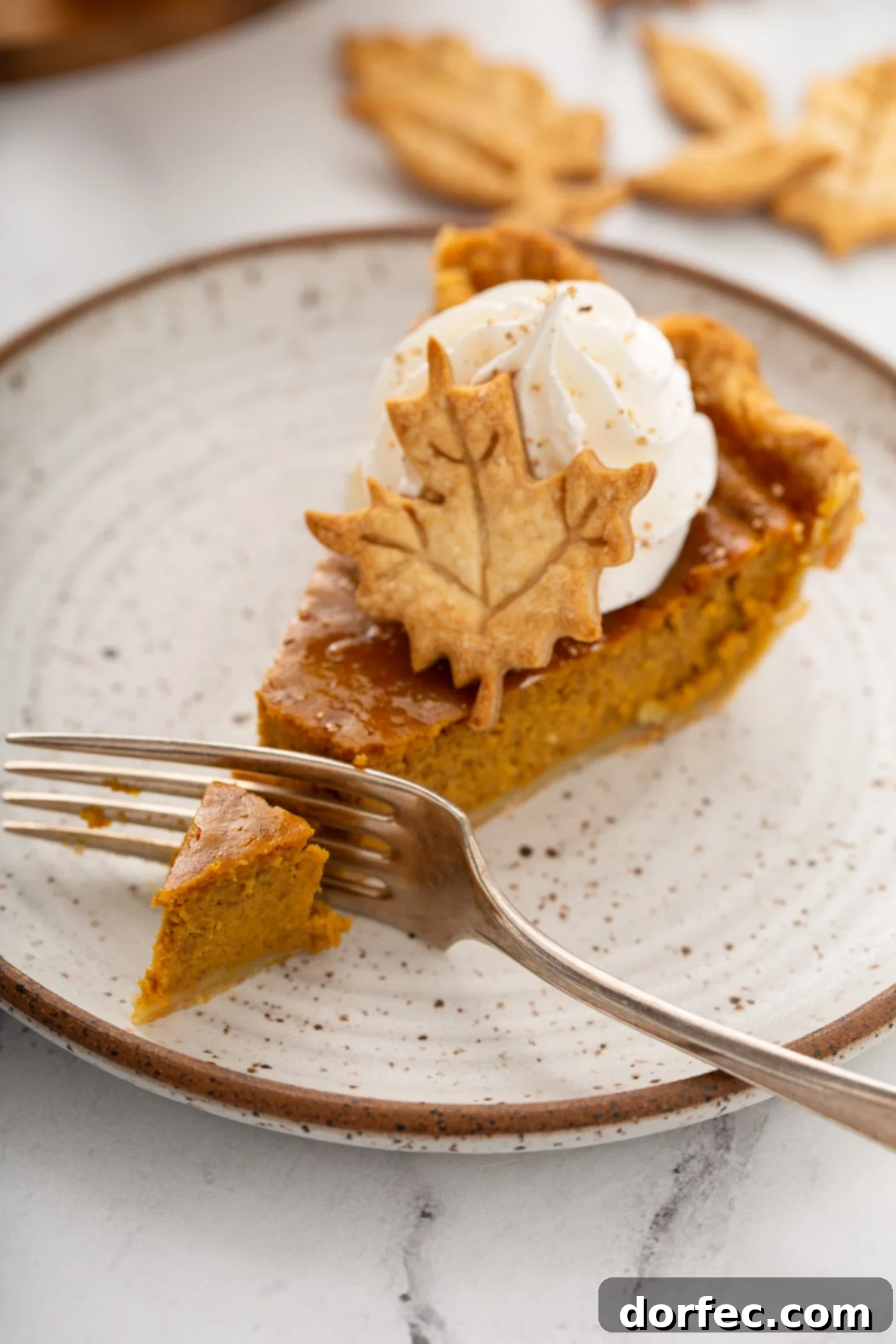 A mesmerizing photo of a single slice of pumpkin pie, a fork poised to take a bite, elegantly topped with piped whipped cream and a delicate pie crust leaf.