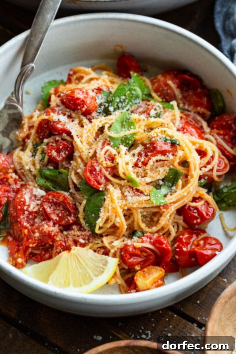 A beautifully plated serving of angel hair pasta, tossed with perfectly sautéed grape tomatoes, fresh basil, Parmesan cheese, and garlic, elegantly accompanied by a bright slice of lemon on the side.