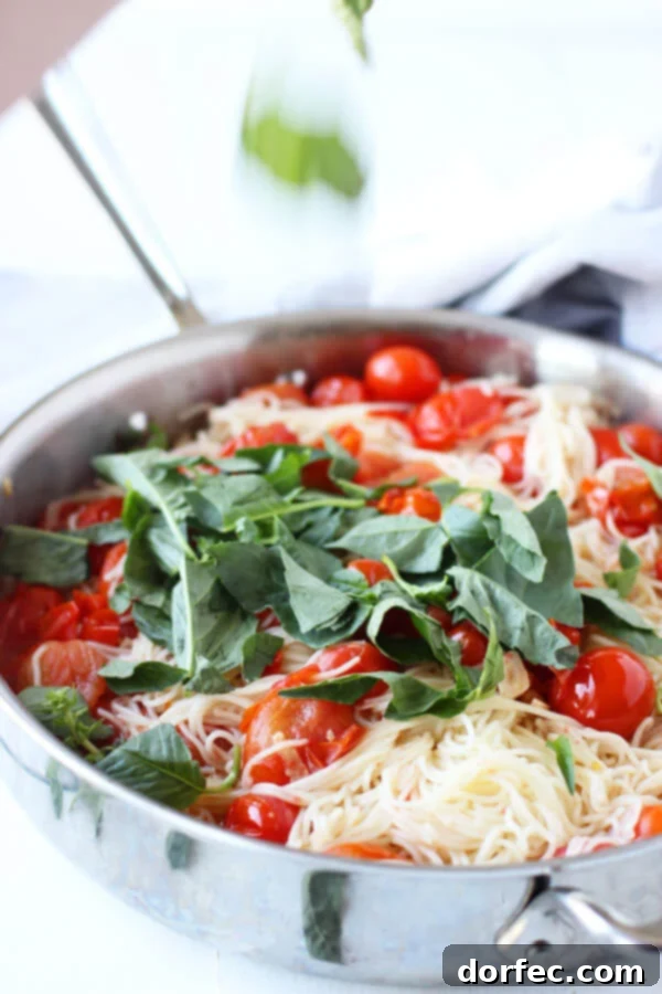 Angel hair pasta, sweet cherry tomatoes, aromatic garlic, and fresh basil cooking together in a stovetop pan.