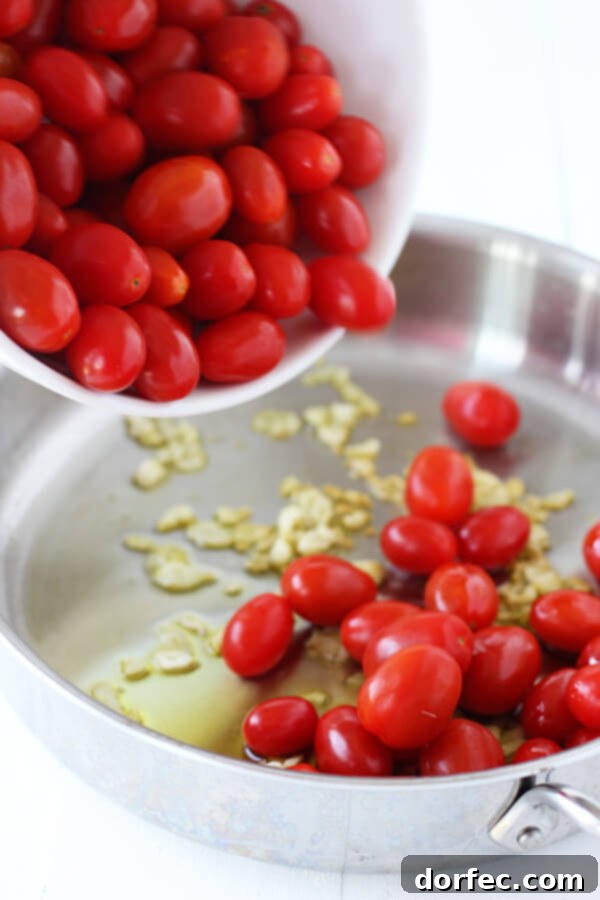 Fresh grape tomatoes being tossed into a hot pan with fragrant garlic and olive oil, beginning the sauce-making process.