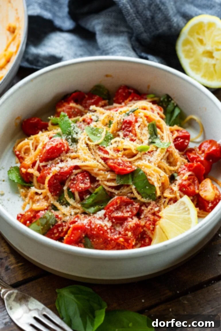 A close-up photo of a bowl filled with cooked angel hair pasta, beautifully tossed with sautéed cherry tomatoes, vibrant fresh basil, and garnished with a slice of fresh lemon.