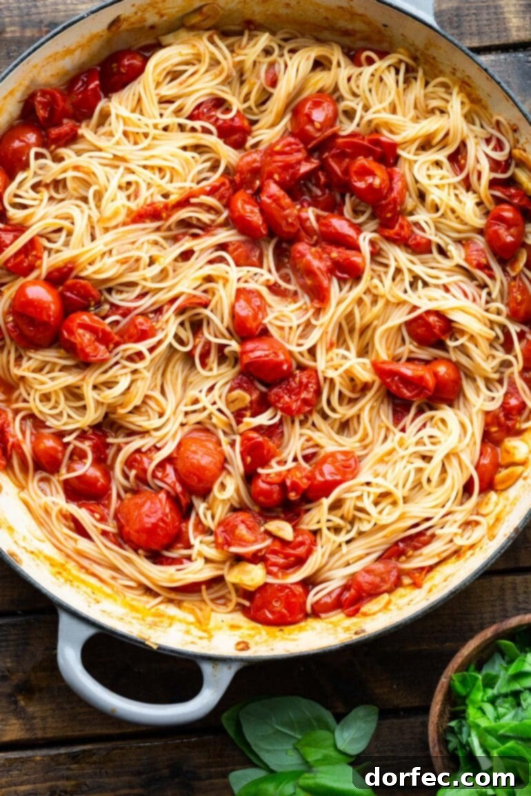 A close-up photo of cooked angel hair pasta after being perfectly tossed with sautéed grape tomatoes and garlic, showcasing the vibrant colors and appealing texture of the dish.
