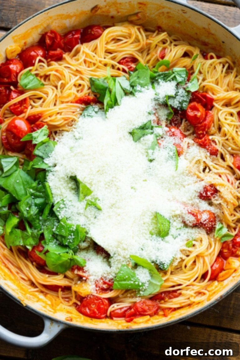 A close-up shot of cooked angel hair pasta, elegantly topped with sautéed grape tomatoes, fresh basil leaves, and a generous sprinkle of granulated Parmesan cheese.