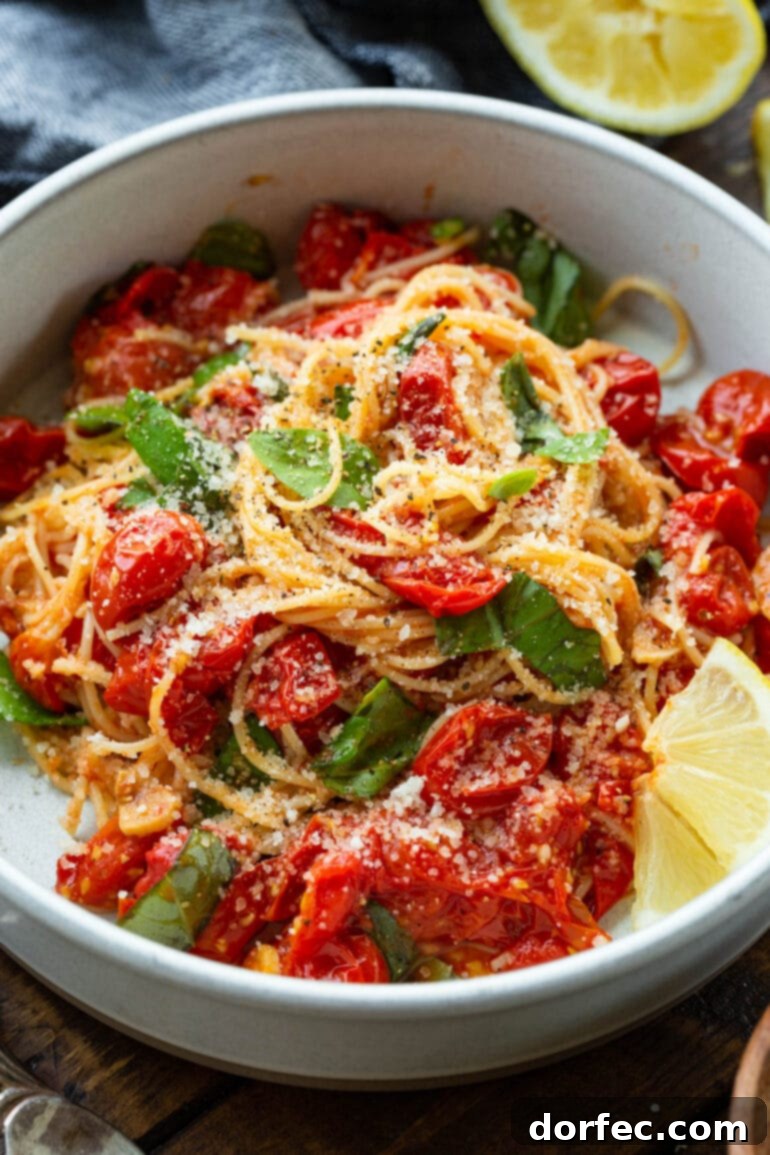 A close-up photo of a bowl filled with angel hair pasta, generously tossed with cooked grape tomatoes, vibrant fresh basil leaves, and topped with a sprinkle of Parmesan cheese.