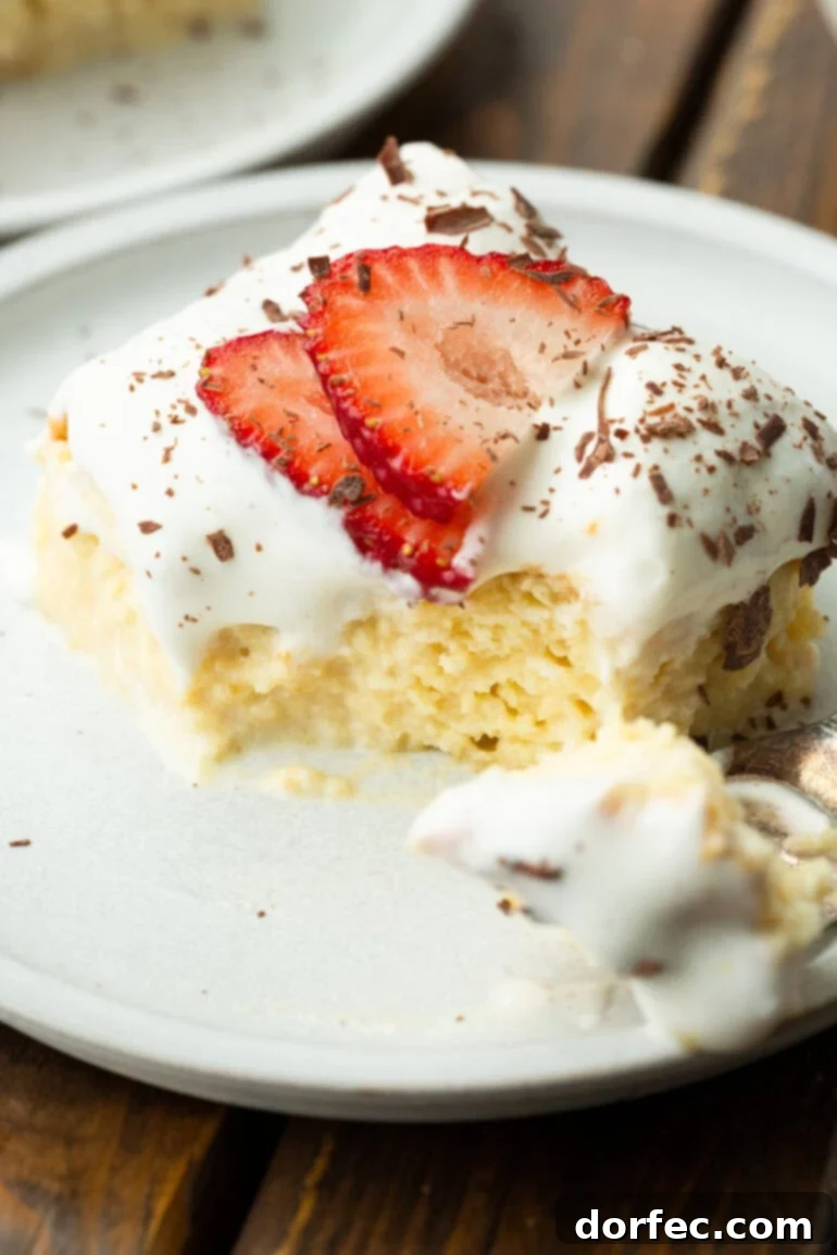 Tres Leches Cake The Creamy Three Milk Delight 3 A photo of a moist piece of Tres Leches cake topped with sliced strawberries and shaved chocolate with a bite removed by a fork, highlighting its rich texture.