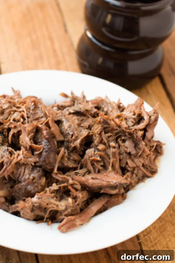 our favorite slow cooker pot roast recipe! ohsweetbasil.com crockpot, insta pot, pressure cooker A serving of tender, shredded slow cooker pot roast on a white plate, garnished with fresh herbs, ready to be served.