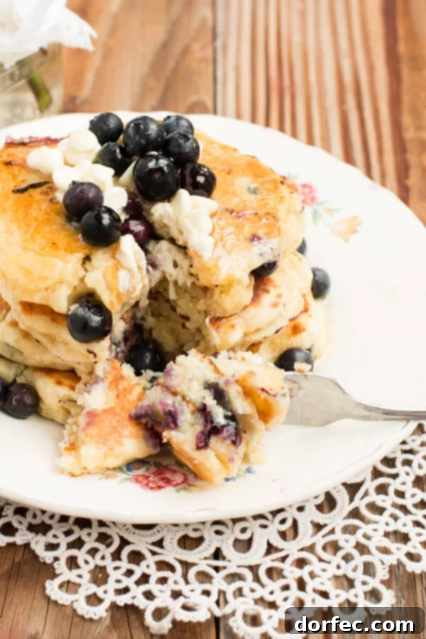 White chocolate blueberry pancakes on ohsweetbasil.com Delicious White Chocolate Blueberry Pancakes stacked high, garnished with fresh blueberries and a drizzle of syrup, ready for a delightful breakfast