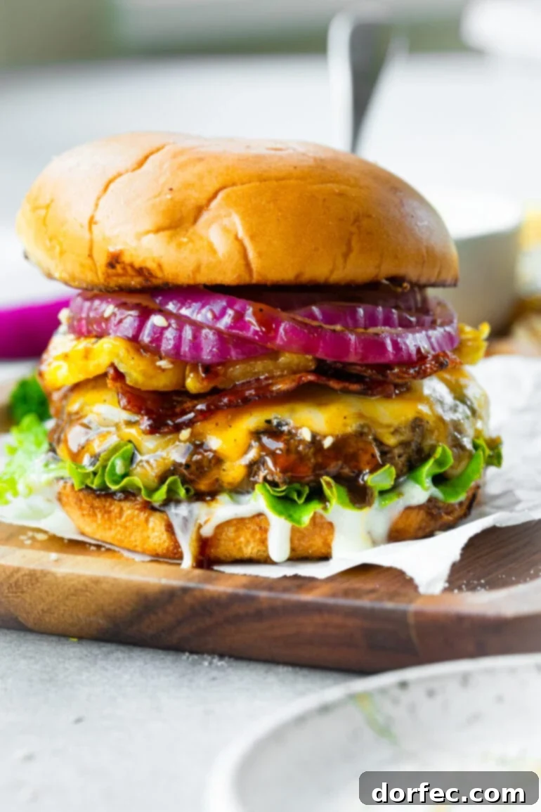 A vibrant cheeseburger stacked high with melted cheese, thinly sliced red onions, a golden grilled pineapple ring, crispy bacon, and a luscious white creamy sauce, all nestled in a perfectly toasted brioche bun.