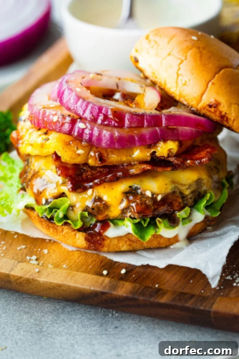 A close-up shot of a perfectly assembled Teriyaki Pina Colada Burger, showcasing a thick, juicy patty, melted Colby Jack cheese, strips of crispy bacon, a grilled pineapple ring, and a generous dollop of the creamy pina colada sauce, with the top brioche bun slightly askew.