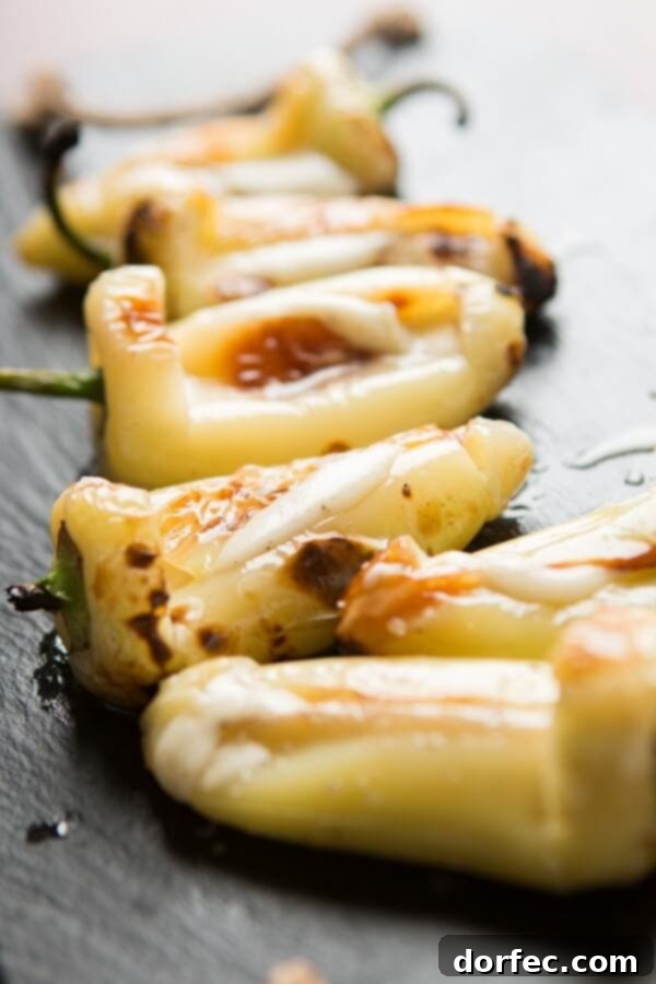 A hand reaching for a grilled cheesy stuffed pepper, emphasizing its appetizer appeal.