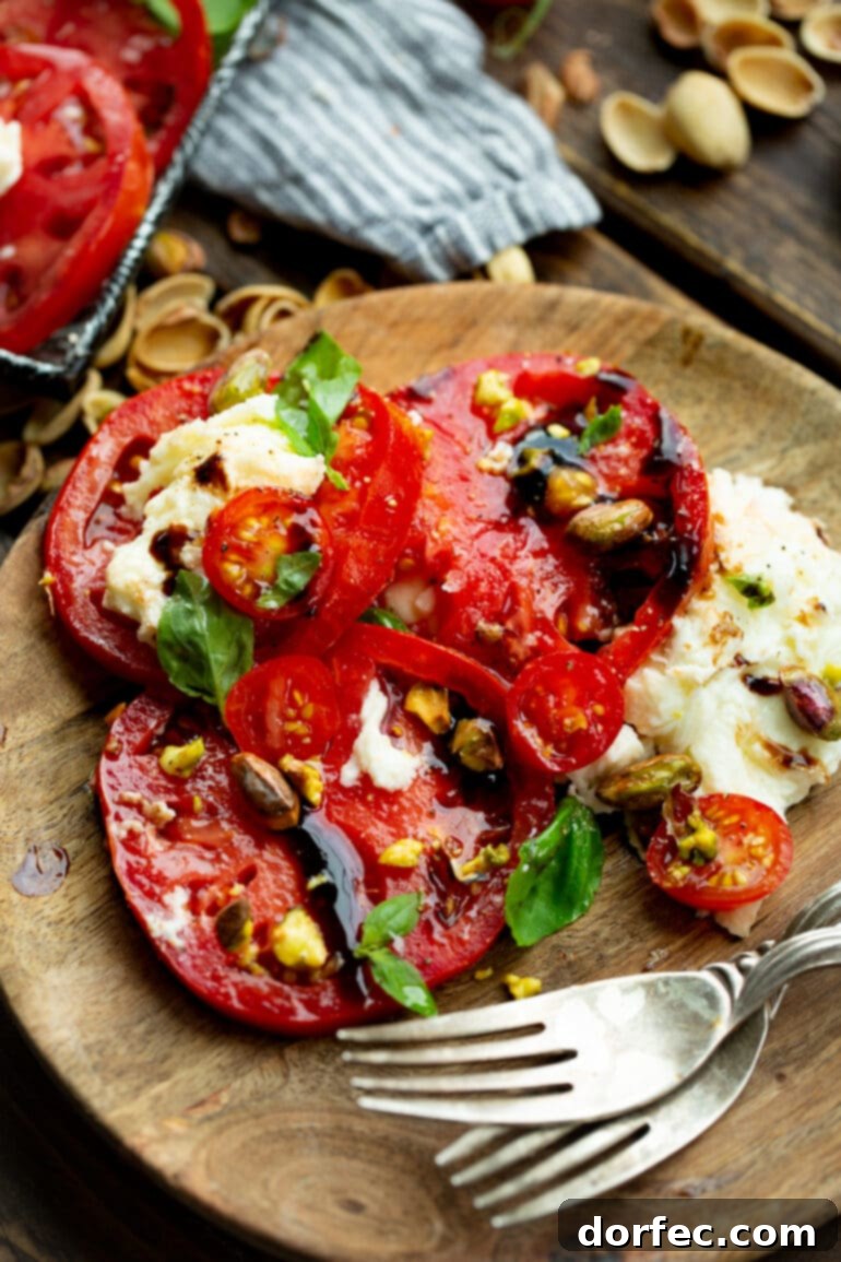 Elevated Caprese Salad with Pistachios 5 A single serving of Caprese salad, elegantly presented on a small wooden plate, showcasing thick slices of tomato and mozzarella, fresh basil, and a generous sprinkle of pistachios with balsamic drizzle.