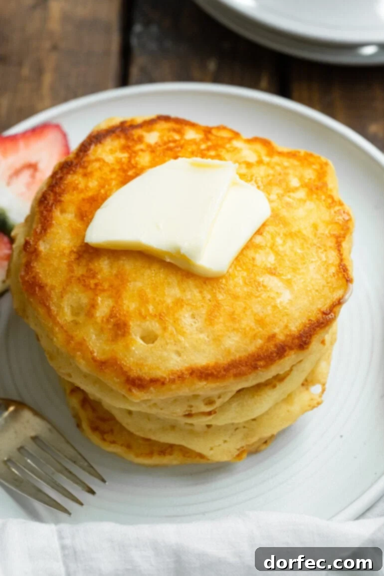 A tall stack of golden, fluffy buttermilk pancakes topped with a pat of melting butter, highlighting their inviting texture.
