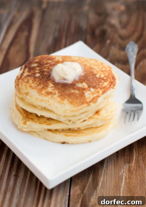 A close-up of a stack of fluffy buttermilk pancakes on a white plate, highlighting their perfectly cooked, golden surface.