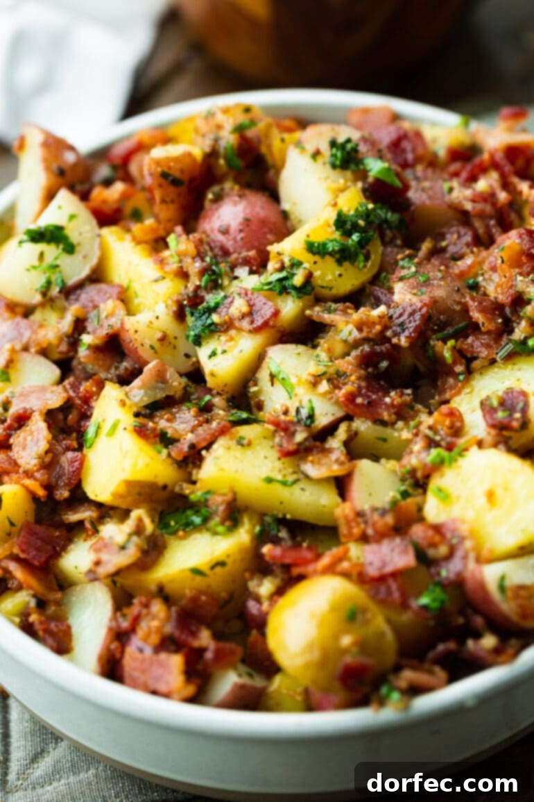a close up photo of a bowl of warm German potato salad full of bacon crumbles, garlic and fresh parsley.
