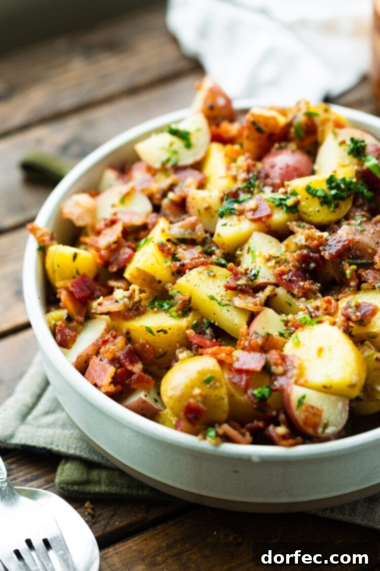 a photo of warm German potato salad loaded with cooked potatoes, crunch bacon crumbles, garlic and parsley.