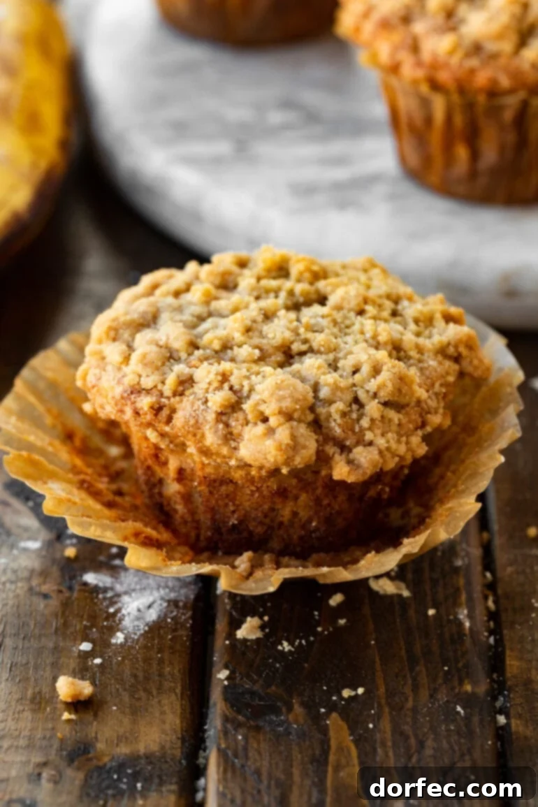 Ultimate Streusel Banana Bread Muffins 2 A perfectly baked banana muffin with a generous, chunky crumb topping. The muffin liner is partially peeled away, revealing the tender, golden-brown sides of the muffin.